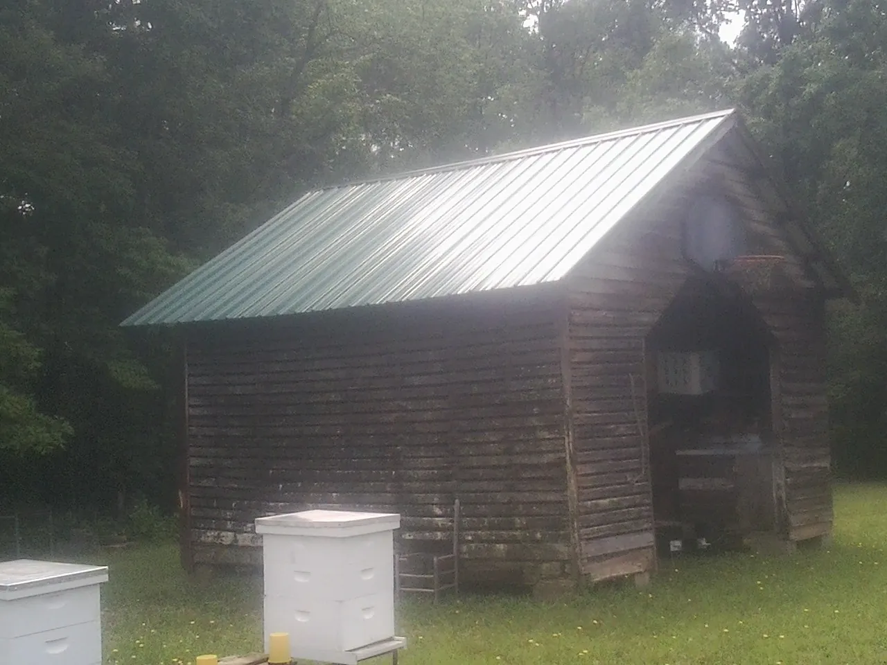 Green metal roof on a weathered barn beside stacked beehives in Waterville