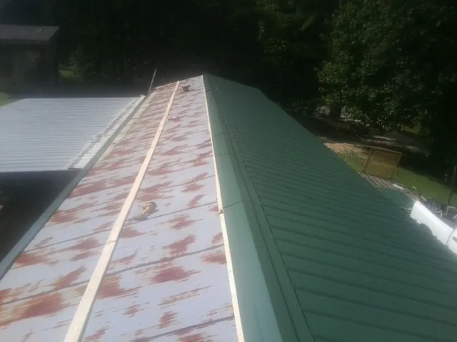 Old rusted panels beside newly installed green metal roofing — Wind Damage Roof Repair by Roofing Brothers in Waterville