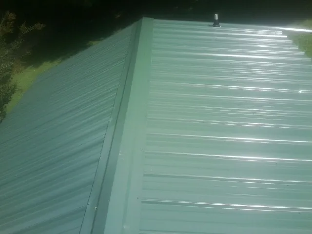 New green metal panels meeting at the ridge of a roof — Flat Roof Repair work by our crew in Waterville